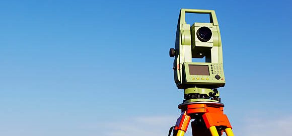Total station - land surveying equipment - mount on tripod on clear blue sky background.